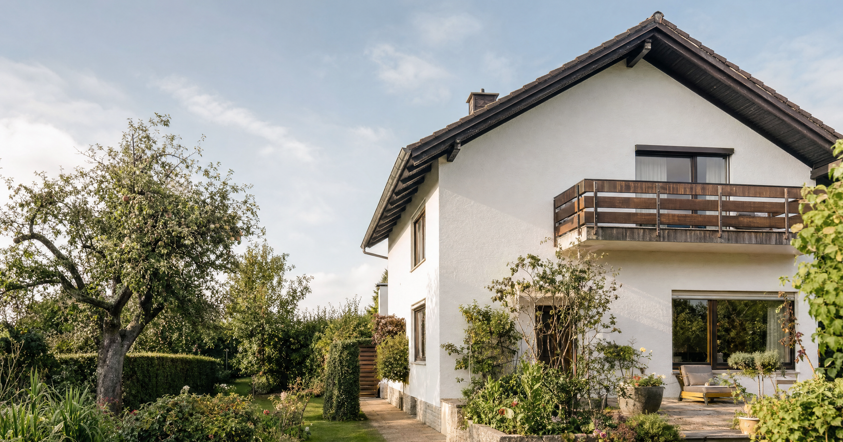 Einfamilienhaus mit weißer Fassade, Holzbalkon und altem Obstbaum im Garten